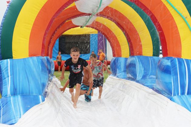 Tate Phillips, Kayden Evans and Johnny Phillips run down the bounce house slip ‘n slide at Mullen Fun Days.