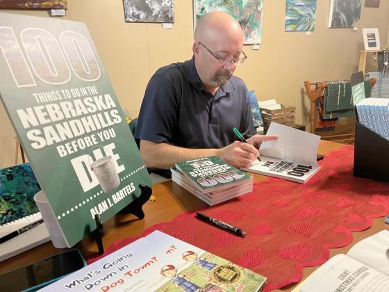 Alan J. Bartels autographs a copy of his new book, “100 Things To Do In The Nebraska Sandhills Before You Die” at the Mullen Arts Center