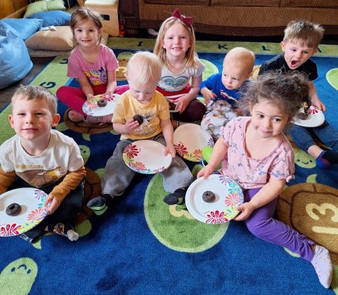 Lots of Love Day Care children with their donuts, l-r: Johnny Phillips, Ryhme Pettit, Mason Deibler, Ryann Walz, Cru Moore, Ellianna Collins, Chasin McIntosh. They are sitting on the rug Lots of Love Day Care was able to purchase from the donations they received at the lemonade stand this past summer. Lori Freeze