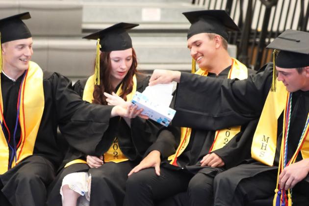 Alex Werner passes the box of Kleenex down to Tate Kvanvig over Trinity Marks and Jacob Walker after the graduates handed out flowers. Gerri Peterson