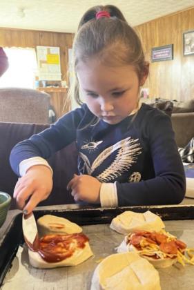 Brogan Jewell (above) spreads her pizza sauce on her pizza. Above right: Chasin McIntosh lounged while he watched Lori make his pizza for him.