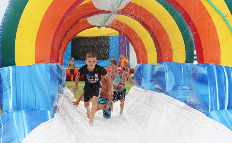 Tate Phillips, Kayden Evans and Johnny Phillips run down the bounce house slip ‘n slide at Mullen Fun Days.
