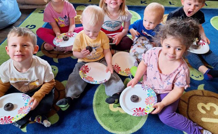 Lots of Love Day Care children with their donuts, l-r: Johnny Phillips, Ryhme Pettit, Mason Deibler, Ryann Walz, Cru Moore, Ellianna Collins, Chasin McIntosh. They are sitting on the rug Lots of Love Day Care was able to purchase from the donations they received at the lemonade stand this past summer. Lori Freeze